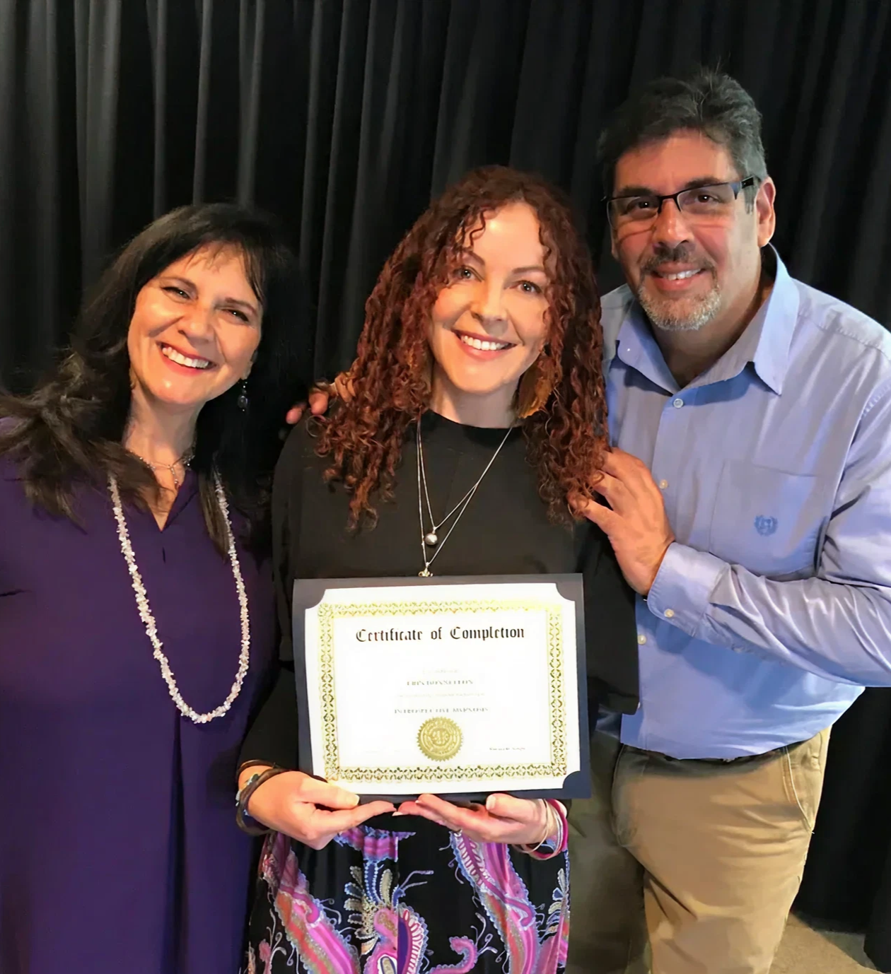 Three people smiling with a certificate.
